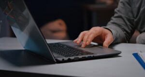 imagem de mão masculina digitando em um notebook que está em uma mesa branca